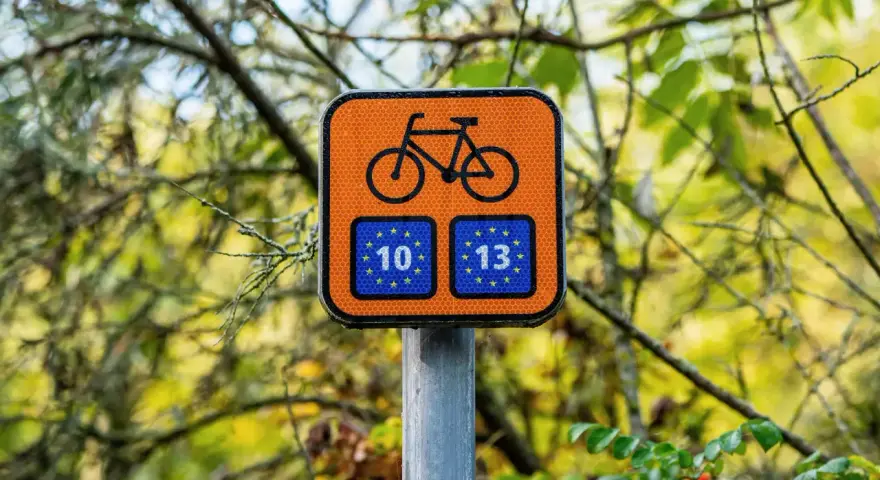 Pomarańczowy znak z rowerem i unijnymi flagami z numerami 10 i 13, wskazujący trasę Euro Velo.