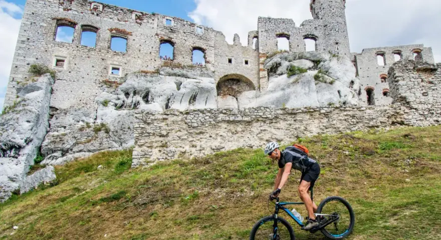 Rowerzysta pokonuje stromy podjazd na tle ruin zamku na Szlaku Orlich Gniazd.