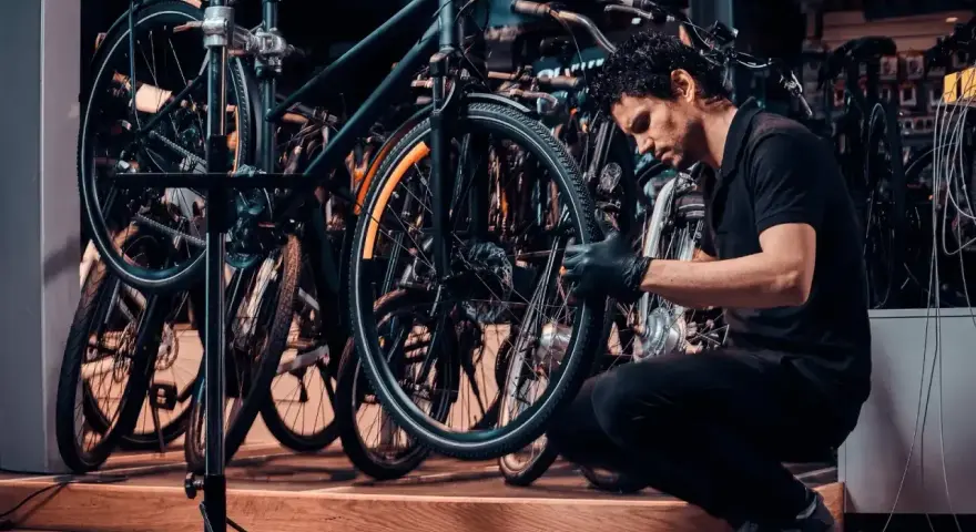 Mechanik w czarnej koszulce i rękawiczkach pokazuje, jak założyć tylne koło w rowerze, pracując w serwisie rowerowym.