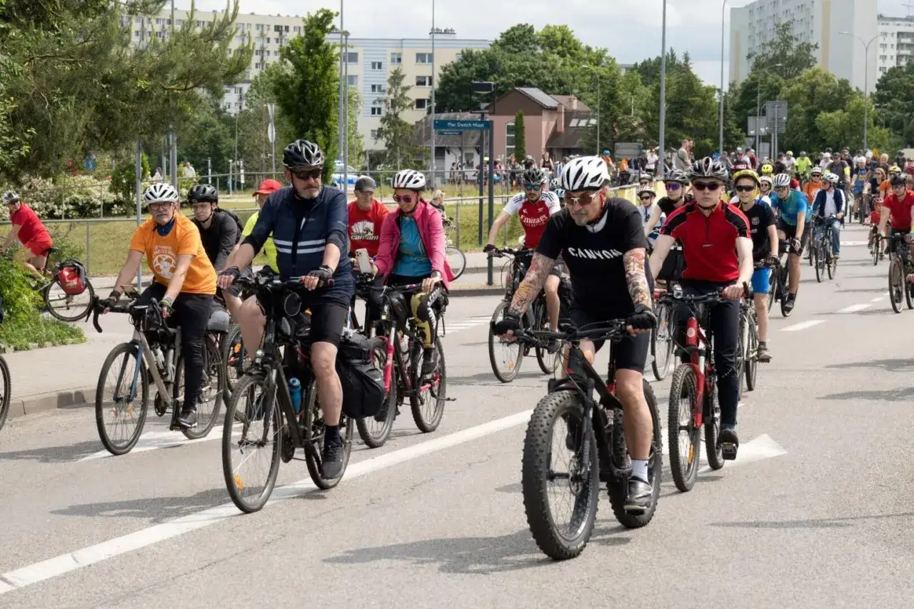 Rowerzyści w kaskach jadą w zorganizowanych grupach rowerowych.