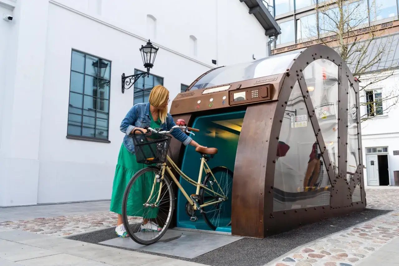 Kobieta z rowerem przy futurystycznej, zautomatyzowanej przechowalni rower&oacute;w. To idealne miejsce przyjazne rowerzystom.