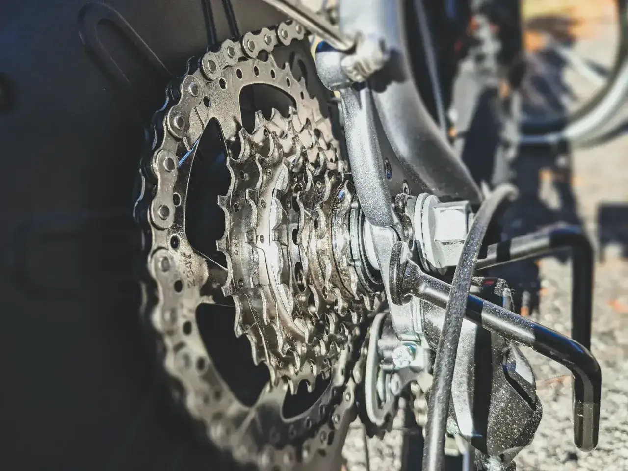Zbliżenie na kasetę rowerową z widocznym przeskakującym łańcuchem w rowerze. Metaliczne ogniwa błyszczą w słońcu.