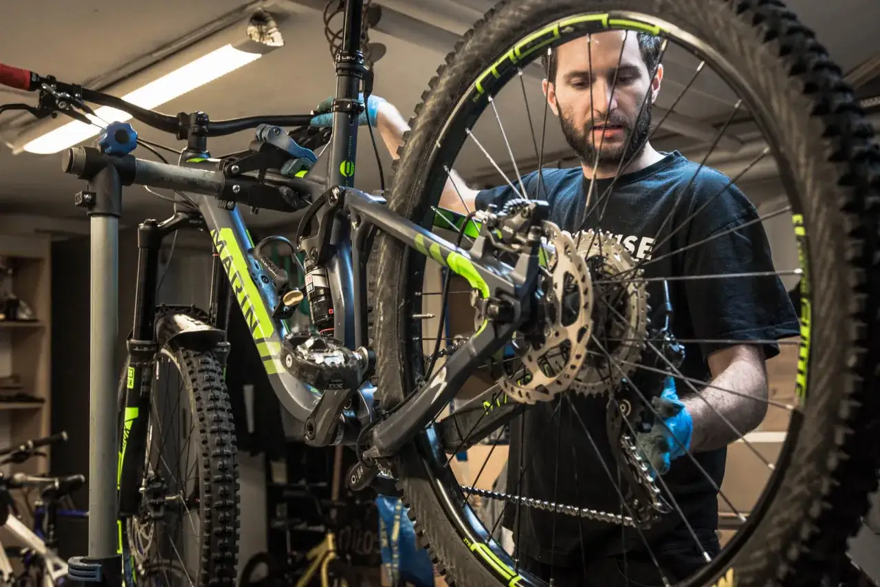 Mechanik w niebieskich rękawiczkach dokonuje wymiany widelca w rowerze g&oacute;rskim.