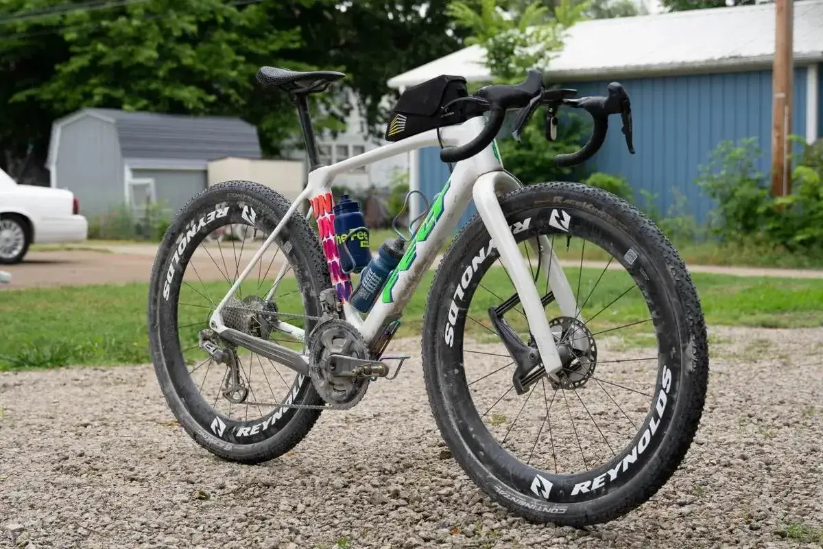 Biały rower gravelowy z szerokimi oponami, gotowy na wyzwania gravel vs mtb. Dwa bidony na ramie.