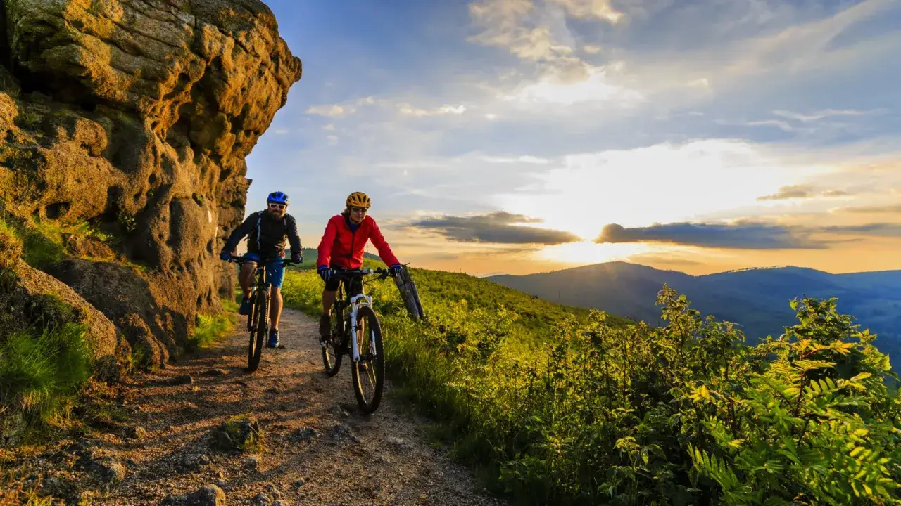 Dwóch rowerzystów na górskim szlaku podczas zachodu słońca. Niezapomniana wyprawa rowerowa wśród skał i zieleni.