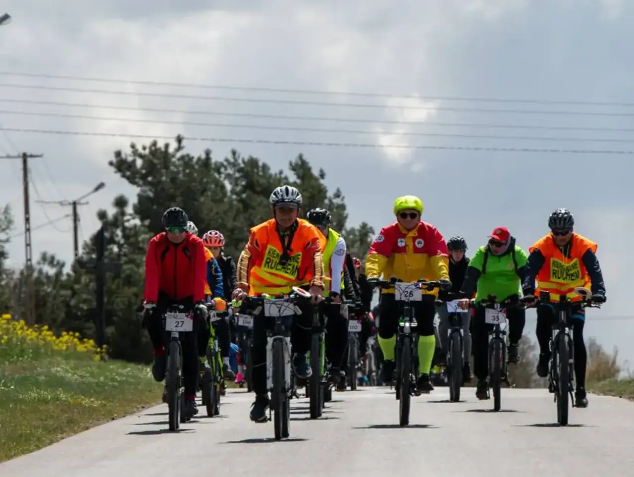 Grupa rowerzyst&oacute;w na trasach rowerowych Kujawsko-Pomorskiego. Kolorowe stroje i kaski, słoneczny dzień.
