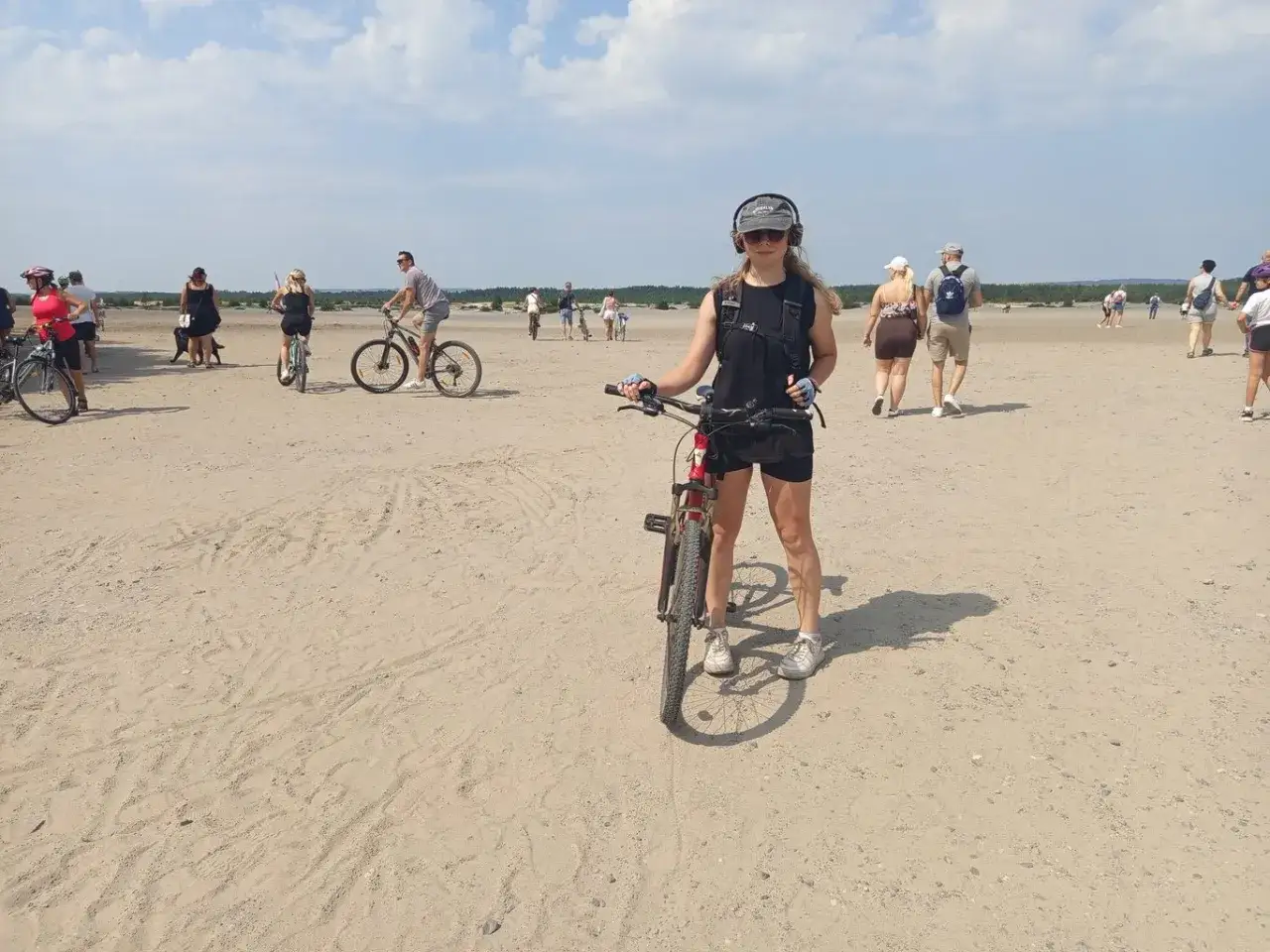 Dziewczyna z rowerem na piaszczystym terenie, gdzie inni też jeżdżą na rowerach i spacerują. To idealne miejsce na velo przemsza.
