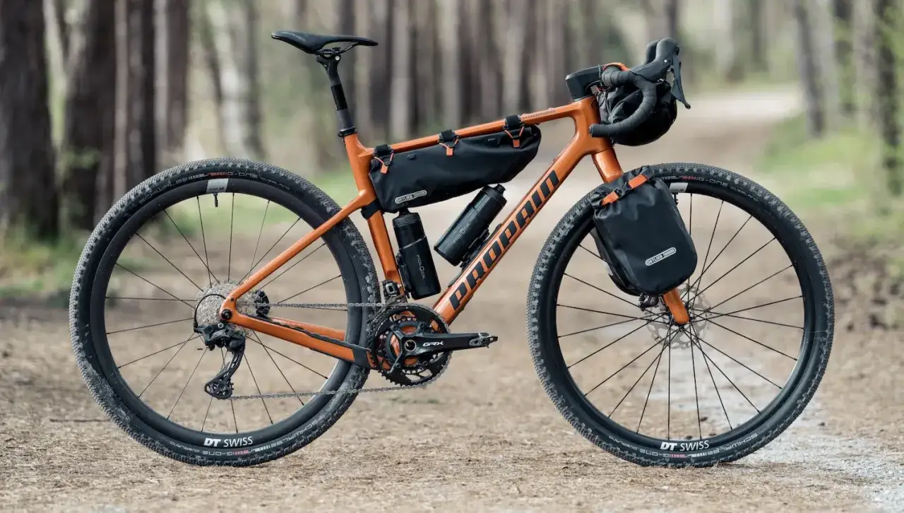 Pomarańczowy rower gravelowy gotowy na bike packing, z sakwami Ortlieb i bidonami.