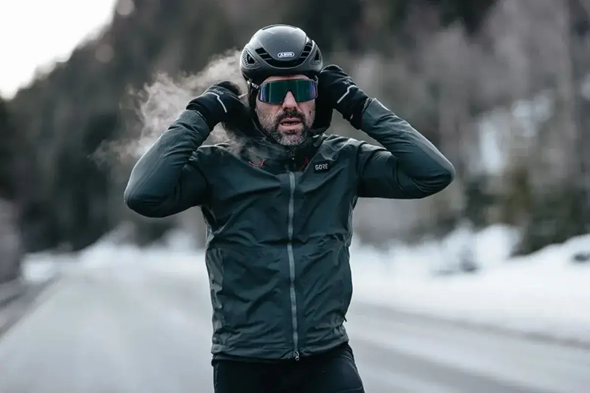 Mężczyzna w kasku i goglach poprawia kaptur ciemnej kurtki GORE-TEX, z kt&oacute;rej unosi się para. Idealna jaka kurtka na zimę dla aktywnych.