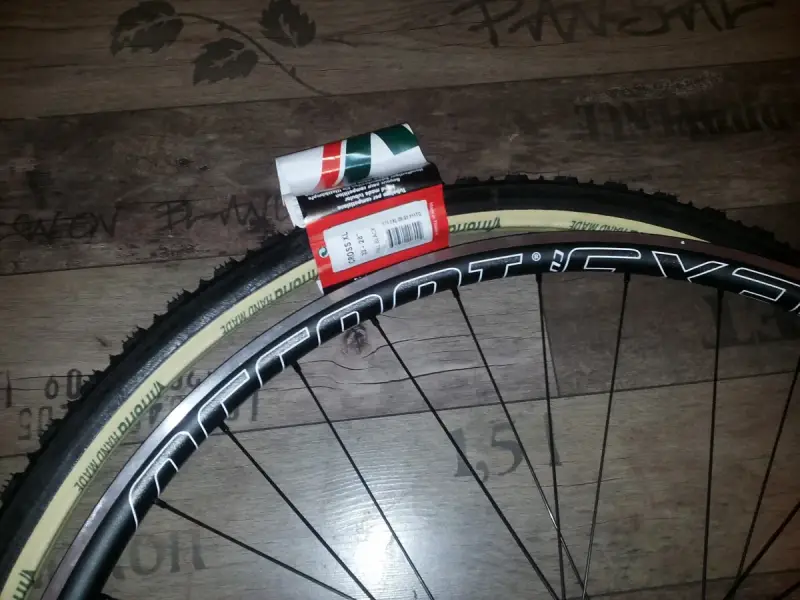 Dwa nowe szytki rowerowe Vittoria Cross XL 33-28" leżą obok czarnej obręczy koła rowerowego.